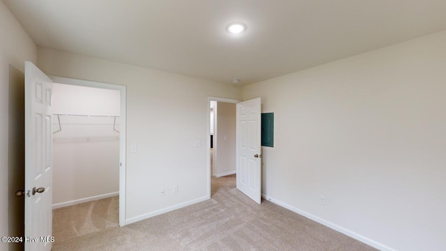 unfurnished bedroom with a closet, electric panel, a spacious closet, and light colored carpet