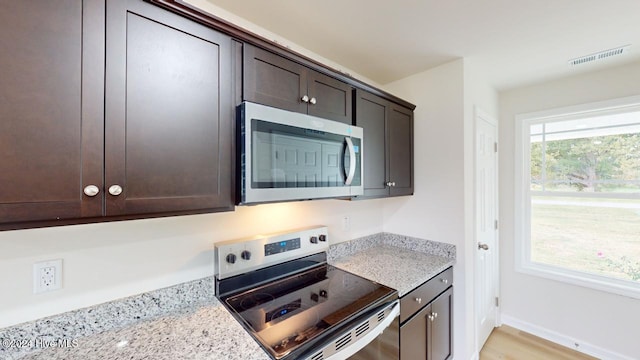 kitchen with light stone countertops, dark brown cabinets, stainless steel appliances, and light wood-type flooring