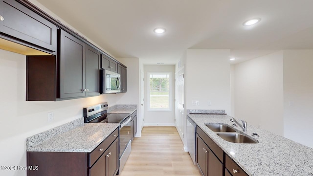 kitchen with sink, light stone counters, dark brown cabinets, appliances with stainless steel finishes, and light wood-type flooring