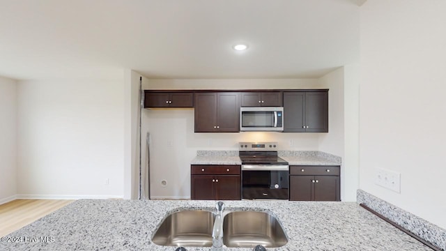 kitchen featuring light stone counters, dark brown cabinets, light hardwood / wood-style floors, and appliances with stainless steel finishes