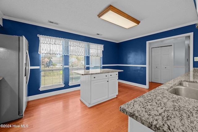 kitchen with light hardwood / wood-style flooring, stainless steel fridge, ornamental molding, a kitchen island, and white cabinetry