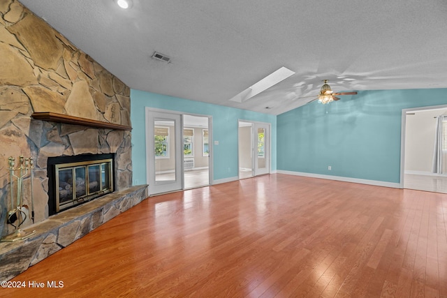 unfurnished living room featuring a stone fireplace, vaulted ceiling with skylight, wood-type flooring, and a textured ceiling