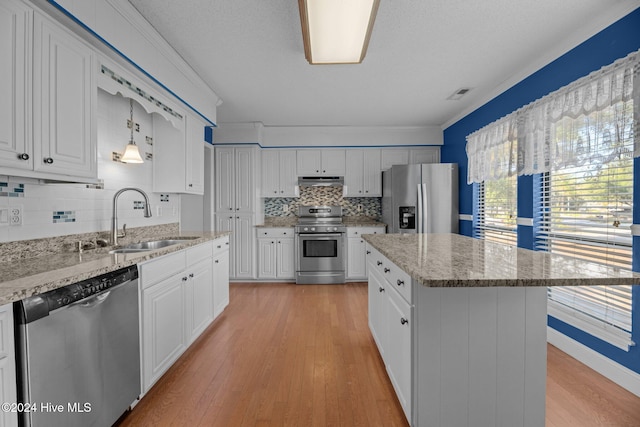 kitchen with appliances with stainless steel finishes, light wood-type flooring, sink, a center island, and hanging light fixtures