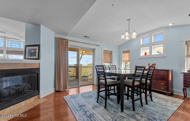 dining room with a fireplace, dark hardwood / wood-style flooring, an inviting chandelier, and vaulted ceiling