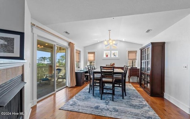 dining area with a tile fireplace, hardwood / wood-style floors, lofted ceiling, and an inviting chandelier