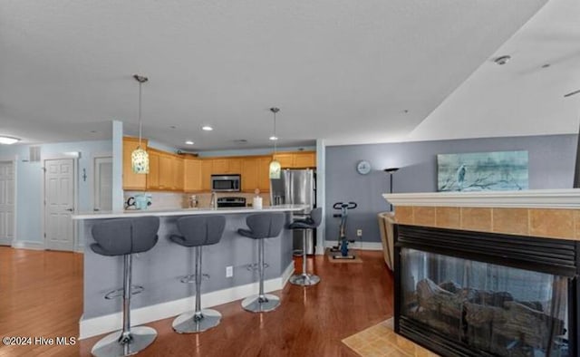 kitchen with hanging light fixtures, hardwood / wood-style floors, a breakfast bar area, a fireplace, and light brown cabinetry