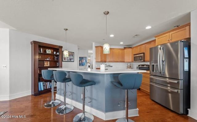 kitchen featuring light brown cabinets, a breakfast bar area, an island with sink, decorative light fixtures, and stainless steel appliances