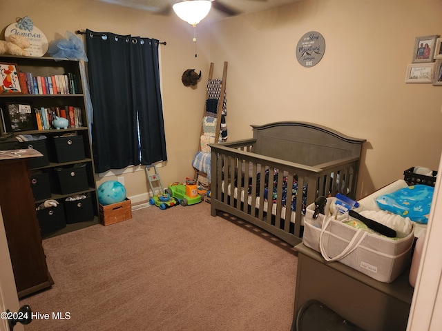 carpeted bedroom with ceiling fan and a nursery area