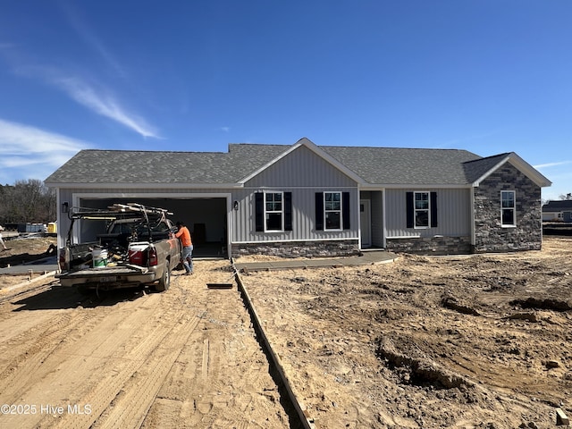 ranch-style home with an attached garage, stone siding, dirt driveway, and roof with shingles