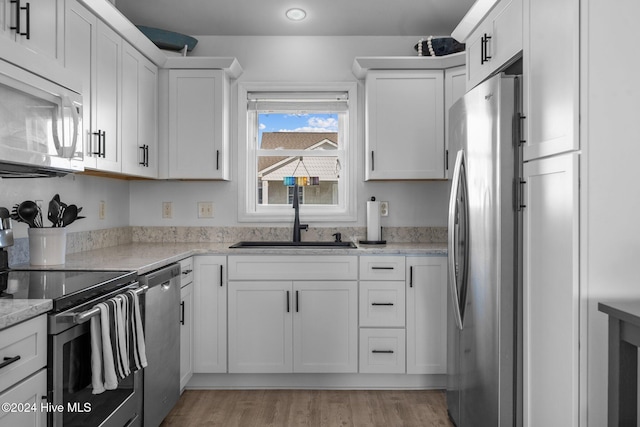 kitchen featuring sink, light hardwood / wood-style flooring, light stone countertops, white cabinetry, and stainless steel appliances