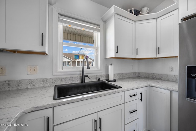 kitchen with light stone countertops, stainless steel fridge with ice dispenser, white cabinetry, and sink