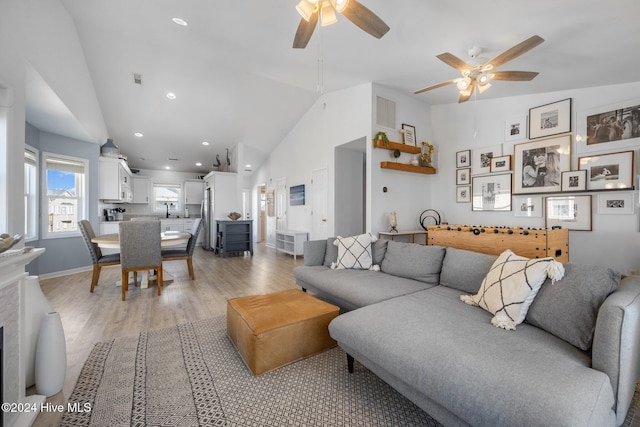 living room with ceiling fan, light hardwood / wood-style flooring, and vaulted ceiling