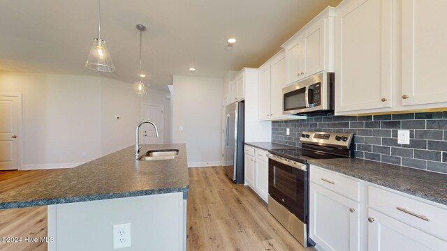 kitchen featuring a center island with sink, decorative backsplash, dark countertops, appliances with stainless steel finishes, and a sink