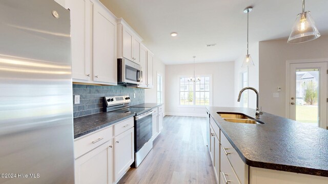 kitchen featuring stainless steel appliances, light wood-style flooring, decorative backsplash, white cabinets, and a sink