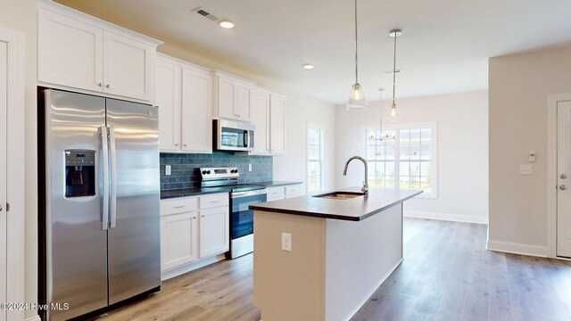 kitchen featuring a center island with sink, stainless steel appliances, dark countertops, backsplash, and a sink