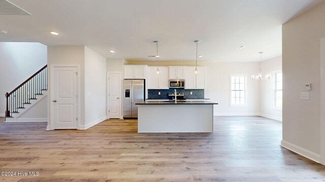 kitchen featuring an island with sink, dark countertops, stainless steel appliances, white cabinetry, and backsplash