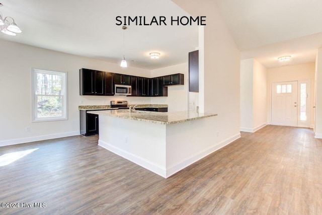 kitchen with wood-type flooring, hanging light fixtures, light stone counters, kitchen peninsula, and stainless steel appliances