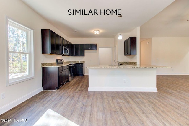 kitchen featuring light wood-type flooring, light stone counters, stainless steel appliances, sink, and pendant lighting