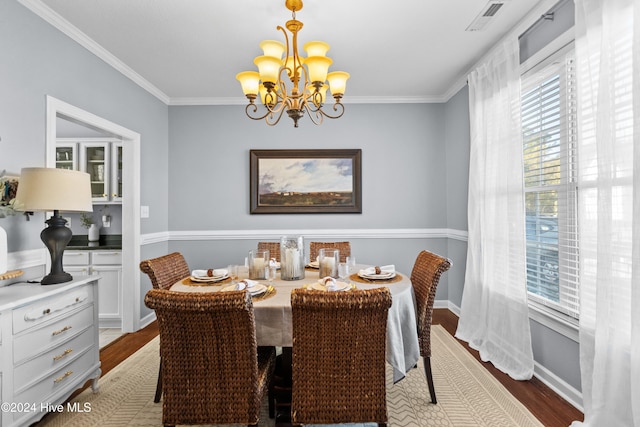 dining space with wood-type flooring, crown molding, and a notable chandelier