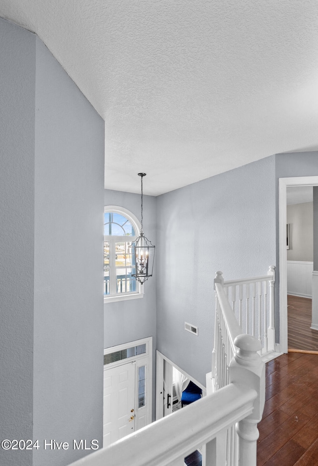 corridor featuring a textured ceiling, an inviting chandelier, and dark wood-type flooring