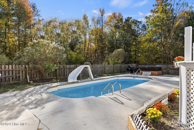 view of swimming pool featuring a patio, a water slide, and a hot tub