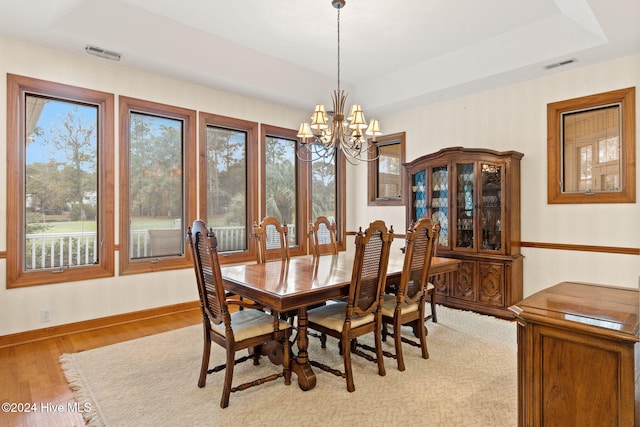 dining area featuring a tray ceiling, light hardwood / wood-style flooring, a wealth of natural light, and an inviting chandelier