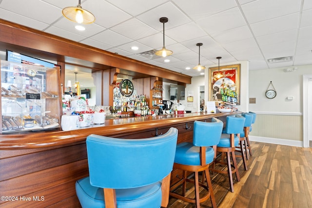 bar with hardwood / wood-style floors, a paneled ceiling, and pendant lighting