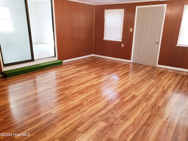 unfurnished room featuring ornamental molding, light hardwood / wood-style floors, and wooden walls