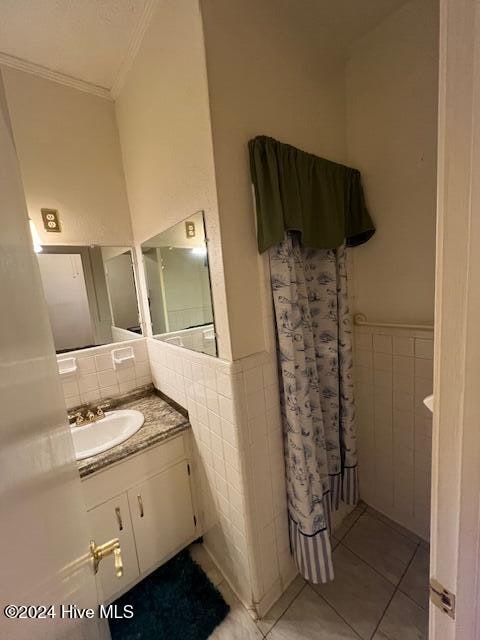 bathroom featuring tile patterned flooring, vanity, ornamental molding, and tile walls