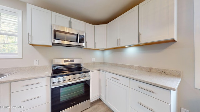 kitchen with white cabinets, appliances with stainless steel finishes, light hardwood / wood-style flooring, and light stone counters