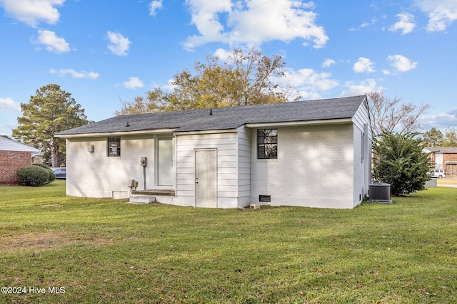 rear view of property with central air condition unit and a lawn