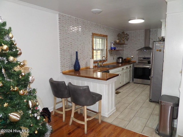 kitchen with sink, wall chimney range hood, appliances with stainless steel finishes, white cabinets, and kitchen peninsula