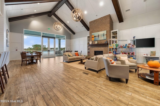 living room with high vaulted ceiling, a chandelier, beam ceiling, light wood-style floors, and a decorative wall