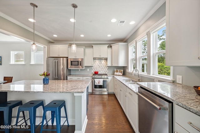 kitchen featuring high end appliances, a sink, crown molding, white cabinets, and a breakfast bar