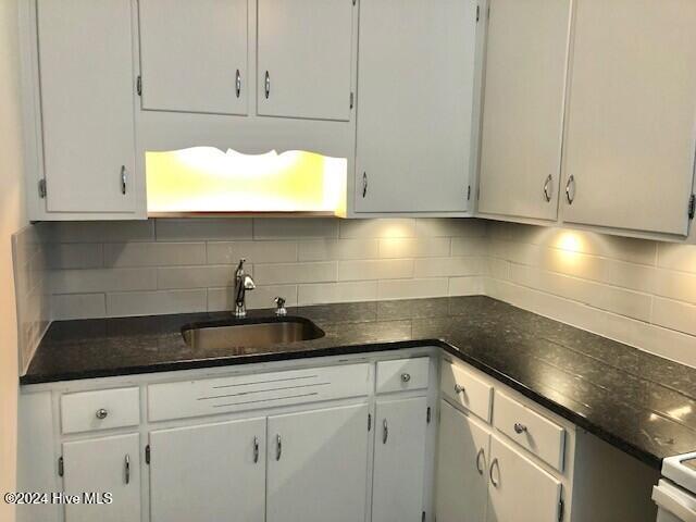 kitchen featuring white cabinets, backsplash, sink, and dark stone counters