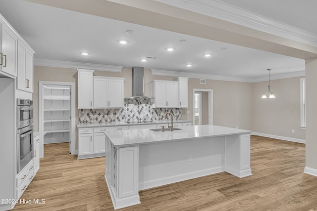 kitchen with wall chimney exhaust hood, light wood-type flooring, white cabinetry, and a kitchen island with sink