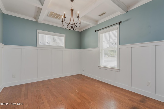 empty room featuring beamed ceiling, a chandelier, light wood-type flooring, crown molding, and coffered ceiling