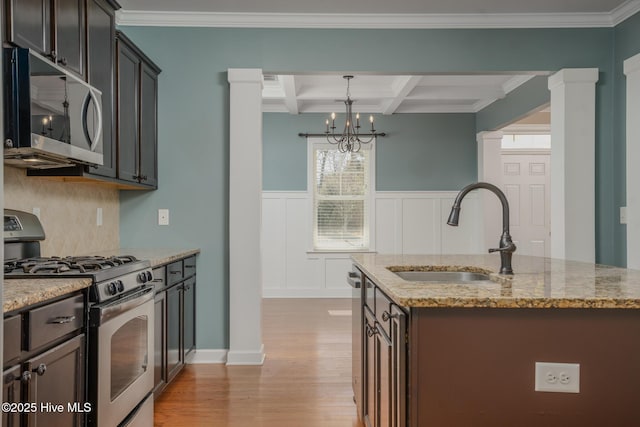 kitchen with appliances with stainless steel finishes, beamed ceiling, an island with sink, sink, and coffered ceiling