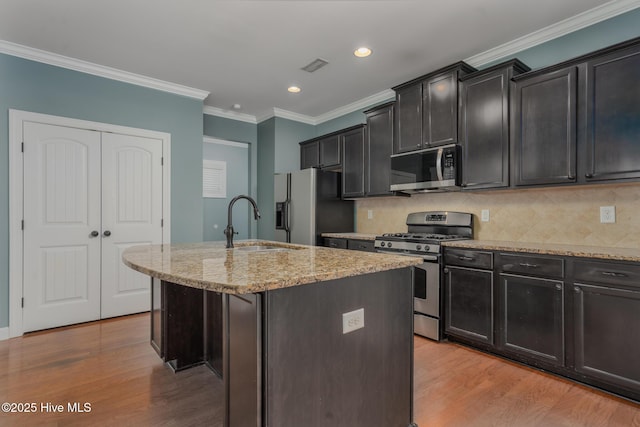 kitchen with light hardwood / wood-style floors, sink, crown molding, appliances with stainless steel finishes, and an island with sink