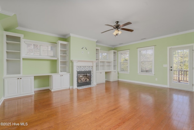 unfurnished living room with ceiling fan, a tile fireplace, crown molding, and light hardwood / wood-style floors