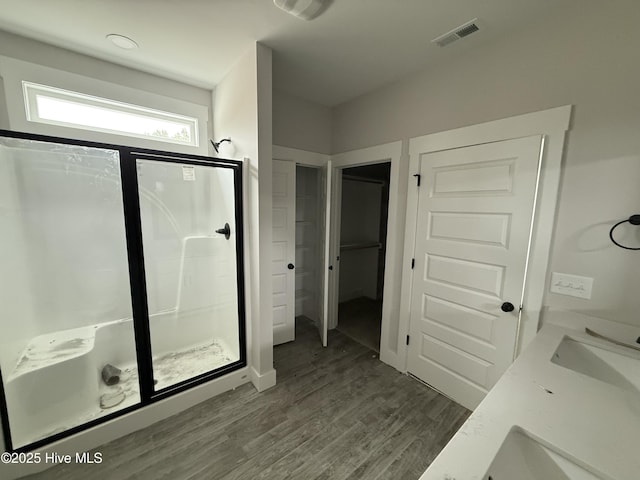 bathroom with a stall shower, wood finished floors, a sink, and a closet