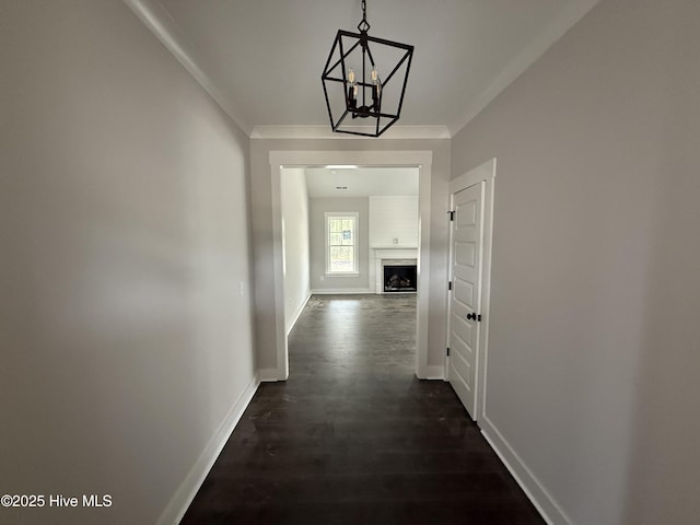 hall featuring a chandelier, crown molding, baseboards, and dark wood-type flooring