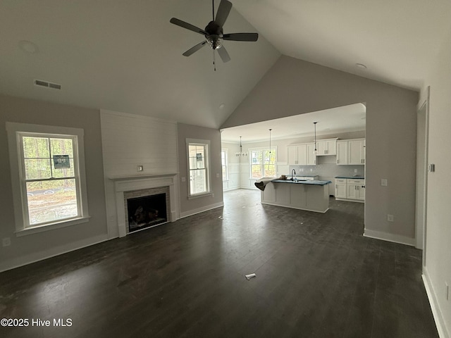 living room with ceiling fan, high vaulted ceiling, a large fireplace, dark wood finished floors, and baseboards