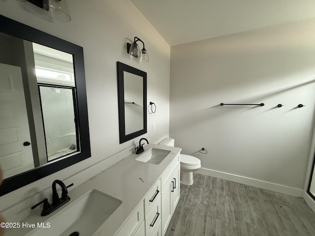 bathroom featuring wood finished floors, toilet, double vanity, and baseboards