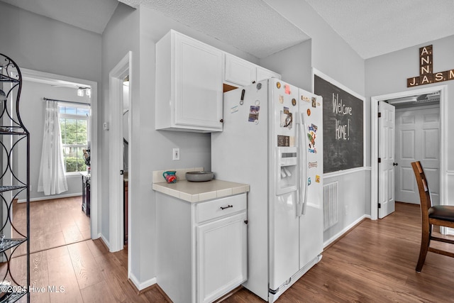 kitchen with a textured ceiling, white cabinetry, white refrigerator with ice dispenser, and hardwood / wood-style flooring