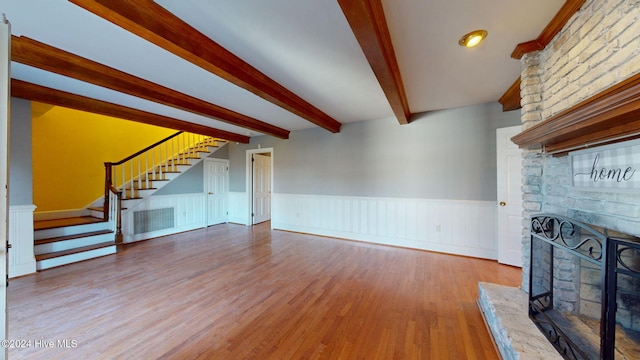 unfurnished living room with beamed ceiling, hardwood / wood-style floors, and a stone fireplace