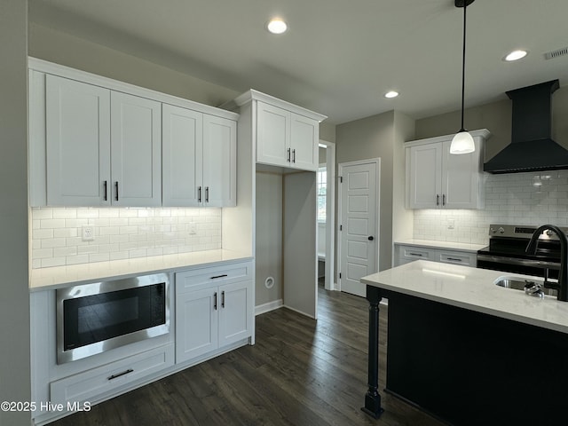 kitchen with a sink, dark wood finished floors, white cabinetry, appliances with stainless steel finishes, and wall chimney exhaust hood