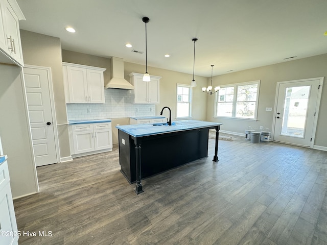 kitchen with pendant lighting, white cabinets, hardwood / wood-style flooring, custom range hood, and a center island with sink