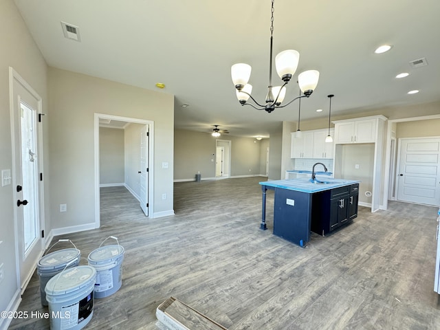 kitchen with decorative light fixtures, white cabinetry, wood-type flooring, an island with sink, and a kitchen bar