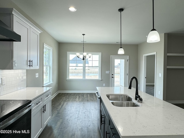 kitchen featuring baseboards, an island with sink, a sink, wall chimney range hood, and backsplash